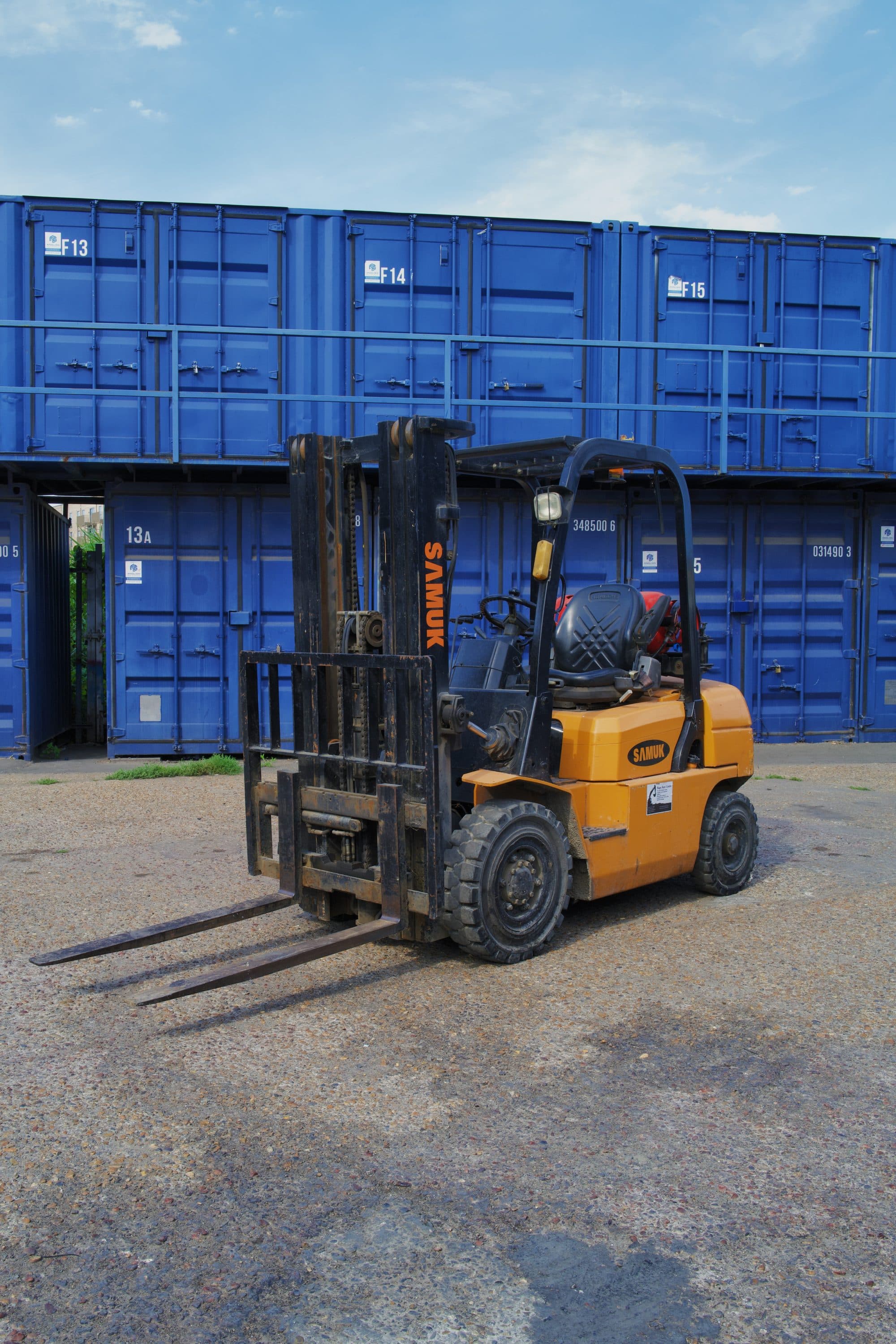 Forklift handling pallets in front of storage containers